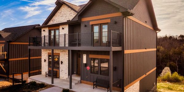Modern two-story house with dark siding and stone accents under a partly cloudy sky.