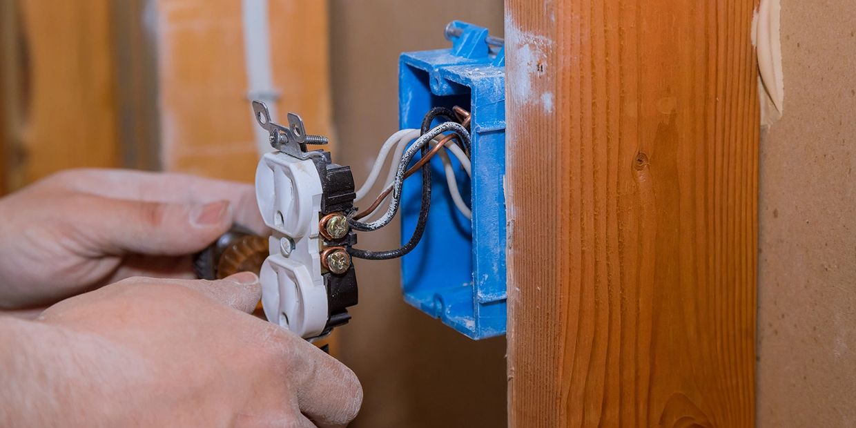 Hands installing an electrical outlet with wires in a blue box.