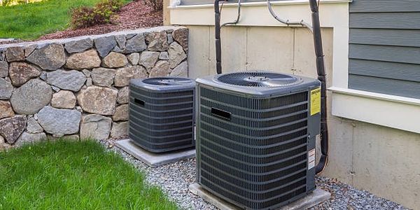Two outdoor air conditioning units installed beside a house with stone wall background.