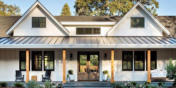 Modern farmhouse with wooden pillars and lush garden in front.