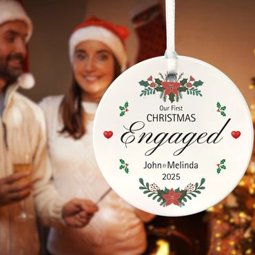 Couple in the background. 3" Ceramic round ornament reads "Our First Christmas Engaged" with names a