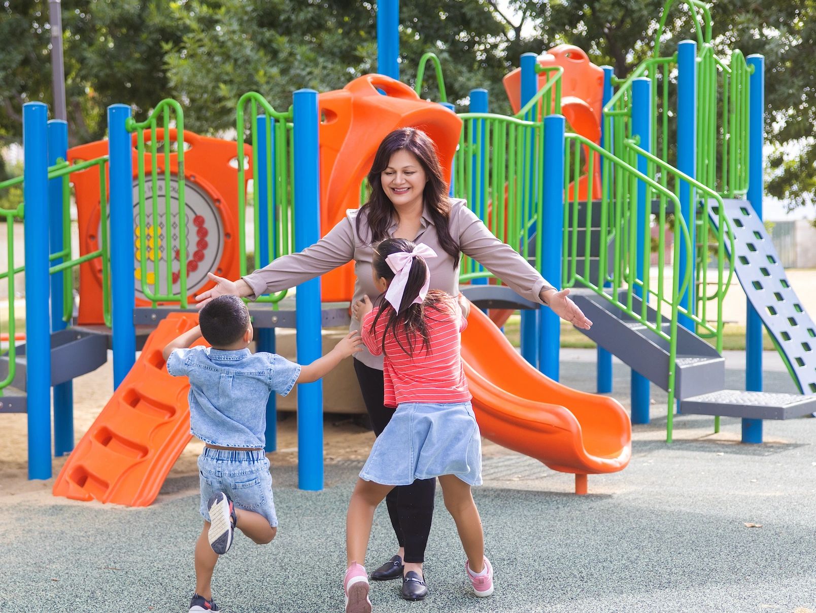 Children running to hug a smiling woman at a playground.