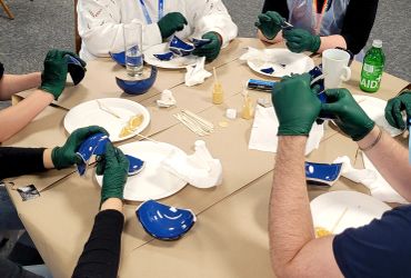 People wearing gloves carefully handling broken blue ceramic pieces at a table.
