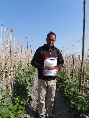 A man holding a container of MacroLiq in a farm field with plants and trellises.