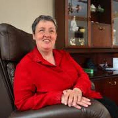 Smiling person in a red shirt seated in a cozy living room with a leather recliner, wooden cabinet,