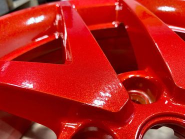 Close-up of a shiny red car wheel rim with a metallic finish.
