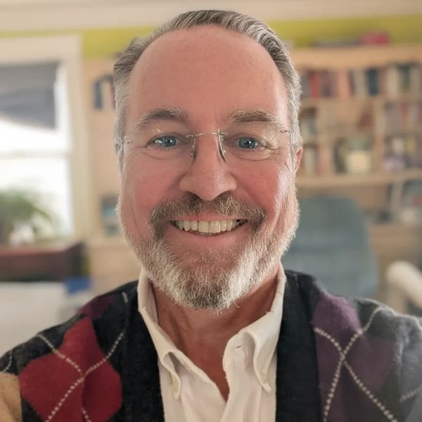 Smiling man with glasses in a cozy, book-filled room.