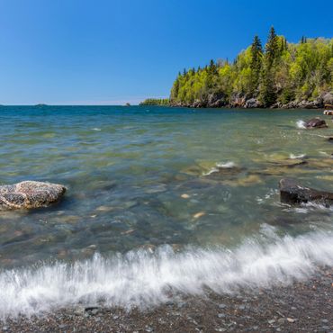 View of Lake Superior's blue waters and gentle waves from a peaceful beach nestled in the forest.