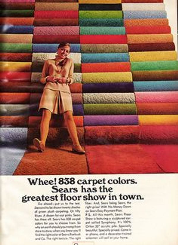 A woman stands smiling against a wall of colorful carpet rolls at Sears.
