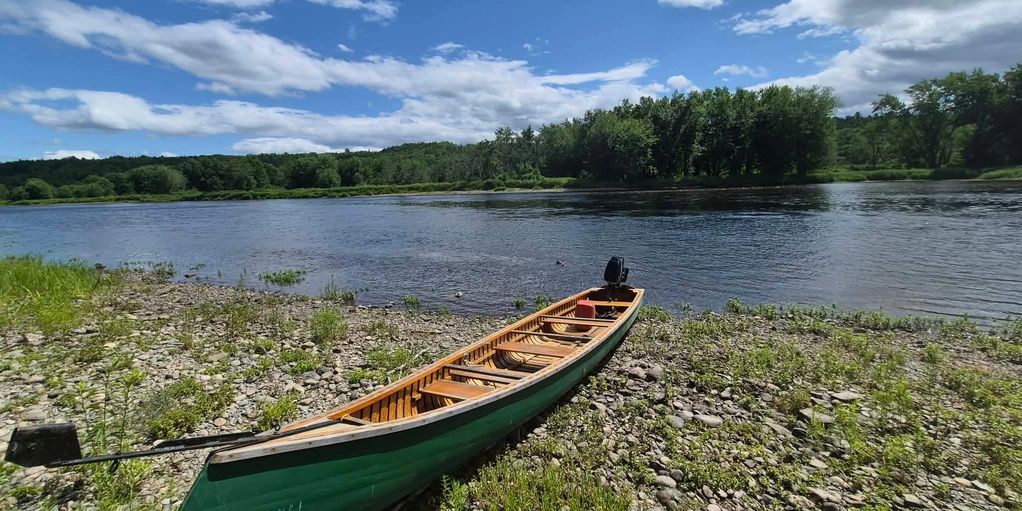 A green canoe by a riverbank on a sunny day.