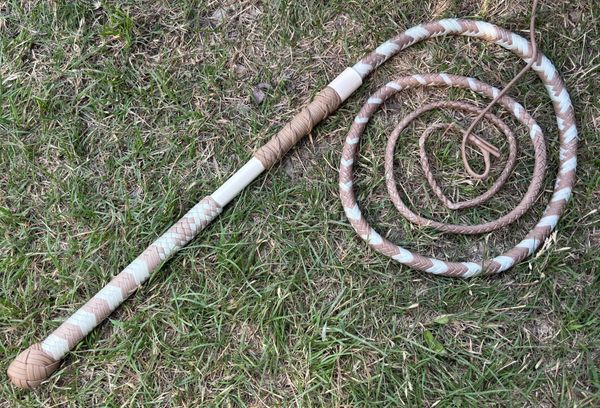 A coiled whip with a woven handle lies on grass.