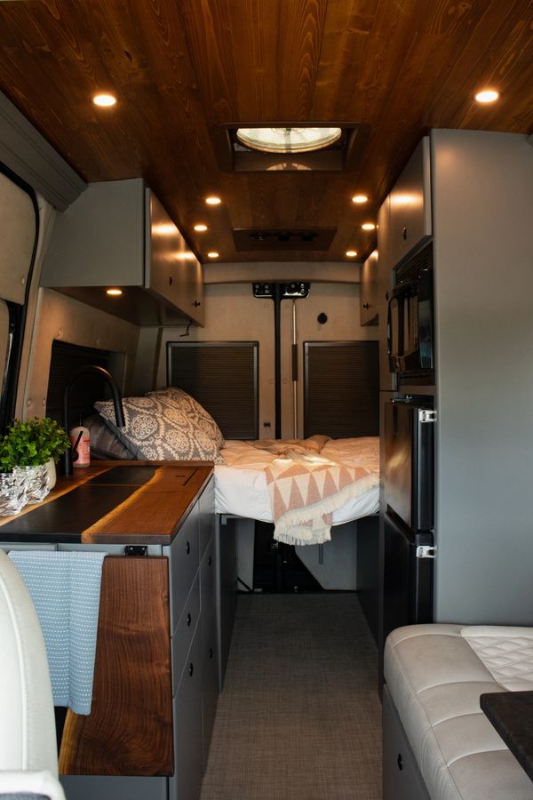 Cozy, modern camper van interior with wood ceiling and compact kitchen.