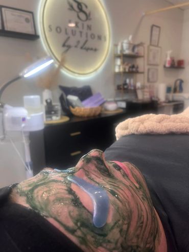 Person relaxing with a facial mask and gel eye patches in a skincare studio.