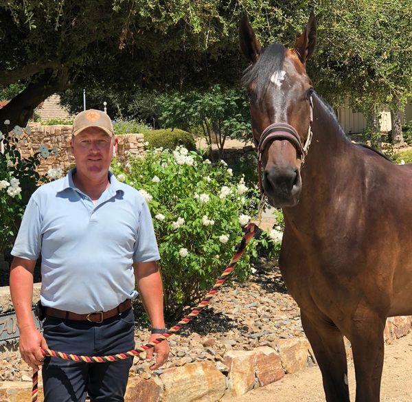 Man standing beside a brown horse holding its lead rope outdoors.