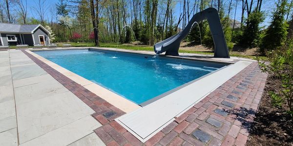 Outdoor swimming pool with a slide and water fountains in a backyard.