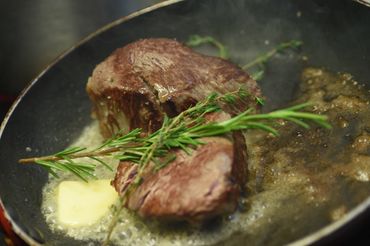 Steak cooking in a pan with butter and fresh herbs.
