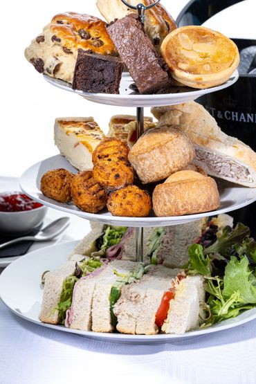 Three-tiered afternoon tea stand with sandwiches, pastries, and scones beside a champagne bucket.