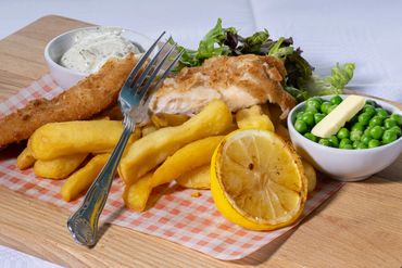 Classic fish and chips served with peas, tartar sauce, and a grilled lemon on a wooden board.