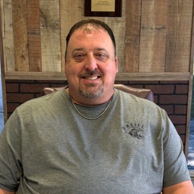 Smiling man wearing a gray t-shirt seated indoors.