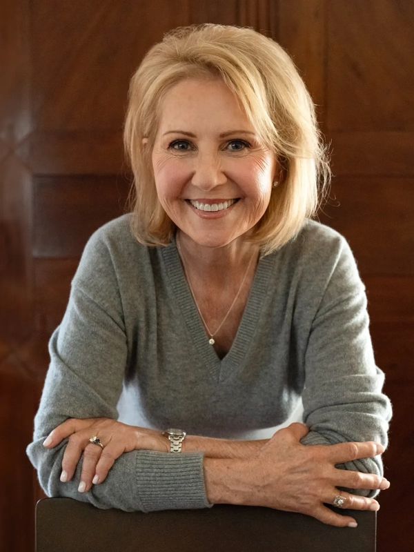 Smiling older woman with blonde hair in a cozy gray sweater.