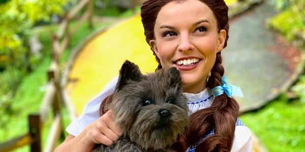 Dorothy from the wizard of oz holding a plush toto dog/ cairn terrier prop