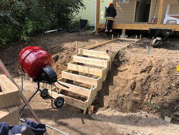 Wooden framework for outdoor stairs under construction with cement mixer nearby.