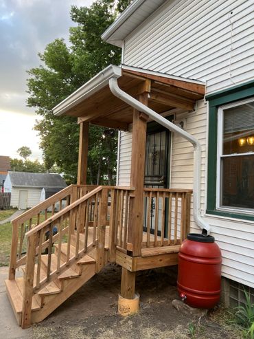 A wooden porch with stairs and a rainwater collection barrel.