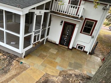 Newly laid stone patio outside a white house with a screened porch and a door decorated with white gloves.