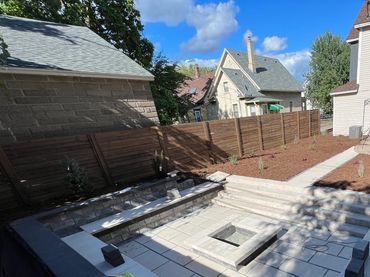 Backyard patio under construction with stone seating and fire pit area.