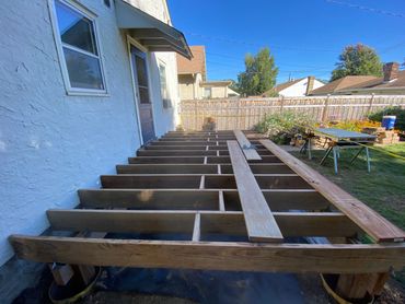 Wooden deck frame under construction beside a house with garden.