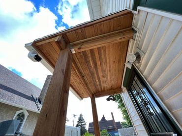 Wooden porch ceiling supported by sturdy beams under a blue sky.