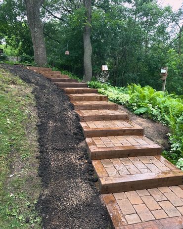 Wooden steps with brick insets lead up a lush, green hillside.