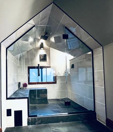 Modern glass shower enclosure with angular design and dark tiles.