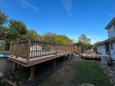 A newly built wooden deck with railing extending from a house to a pool.
