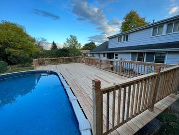 Newly built wooden deck surrounding an above-ground pool beside a house.
