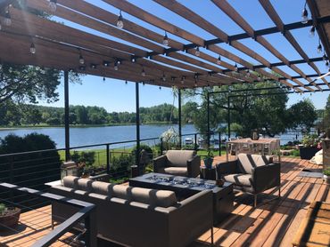 Spacious deck with seating and dining area overlooking a serene lake under a clear sky.