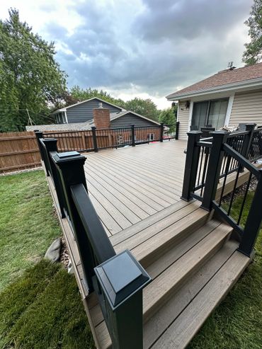 Newly built wooden deck with black railing on a cloudy day.