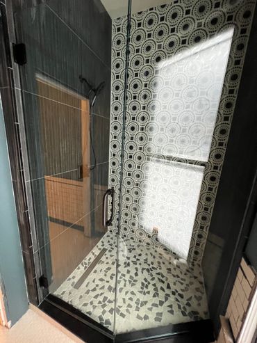 Modern shower with patterned tiles and mosaic floor inside glass enclosure.