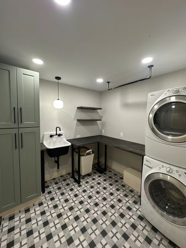 Modern laundry room with stacked washer and dryer, utility sink, and patterned floor tiles.