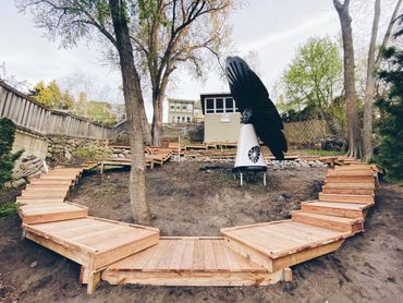 Curved wooden steps surround a smartflower solar panel in a backyard.