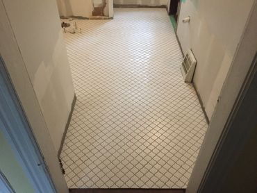 Newly tiled bathroom floor with white patterned tiles and unfinished walls.