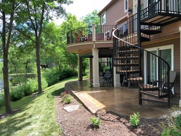 Outdoor patio with spiral staircase and greenery by a lake.