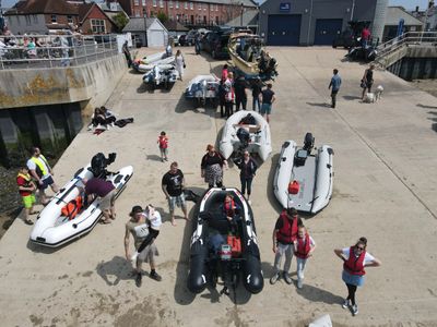 People and inflatable boats gathered at a harbor dock on a sunny day.