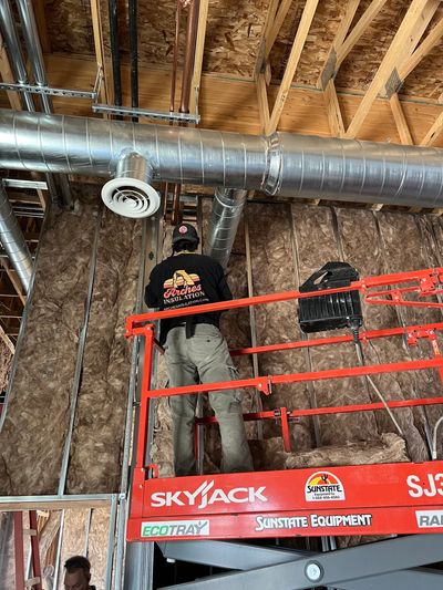Worker on lift installing insulation and ductwork in construction site.
