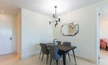 Minimalist dining area with a wooden table, four chairs, geometric chandelier, and mirrored wall decor.