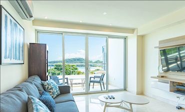 Bright living room with modern furniture and a balcony view of greenery and water.