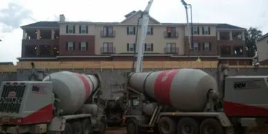 Concrete mixers at a construction site in front of a large apartment building.