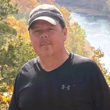 Man wearing a cap standing outdoors near a river.