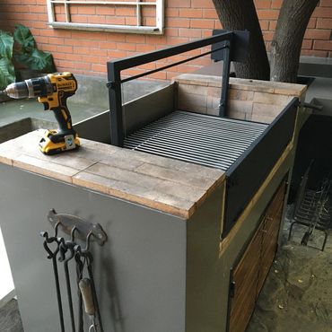 Modern outdoor grill with tools and a cordless drill on top.