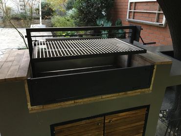 Outdoor grill with adjustable metal grate and hand crank in backyard.